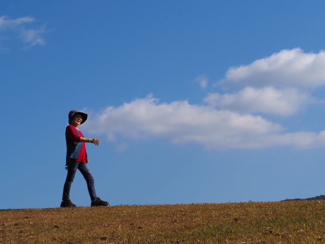 青空と白い雲をバックに歩く高齢女性